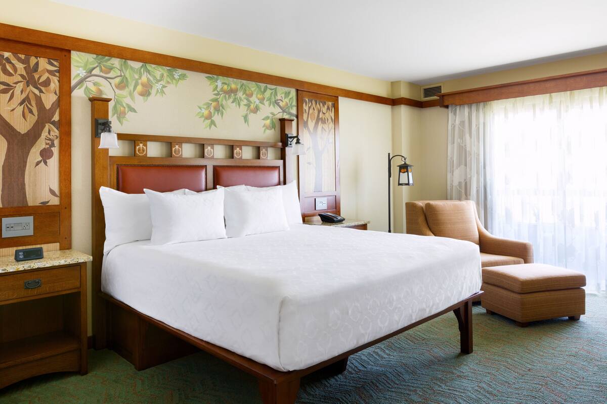 Een hotelkamer met een groot bed, een houten hoofdeinde, een nachtkastje, een stoel en een muurschildering.