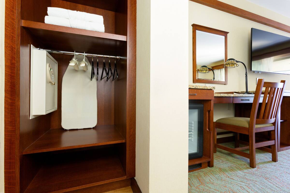 Een hotelkamer met een houten garderobe, een bureau met een televisie en een stoel.