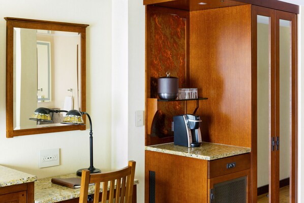 Cocina compacta con mostrador, cafetera, olla y un espejo sobre el lavamanos.
