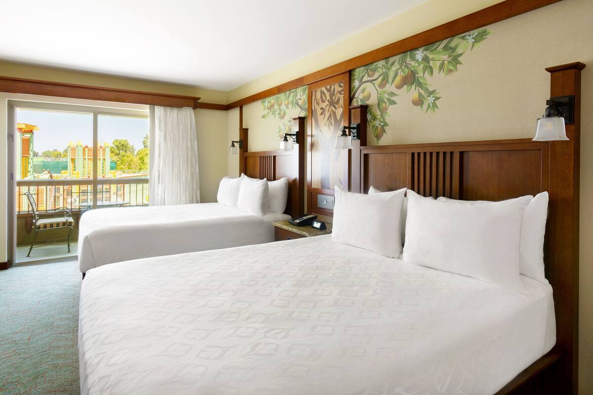 Een hotelkamer met twee bedden, een balkon en een uitzicht, plus een decoratief muurschildering.