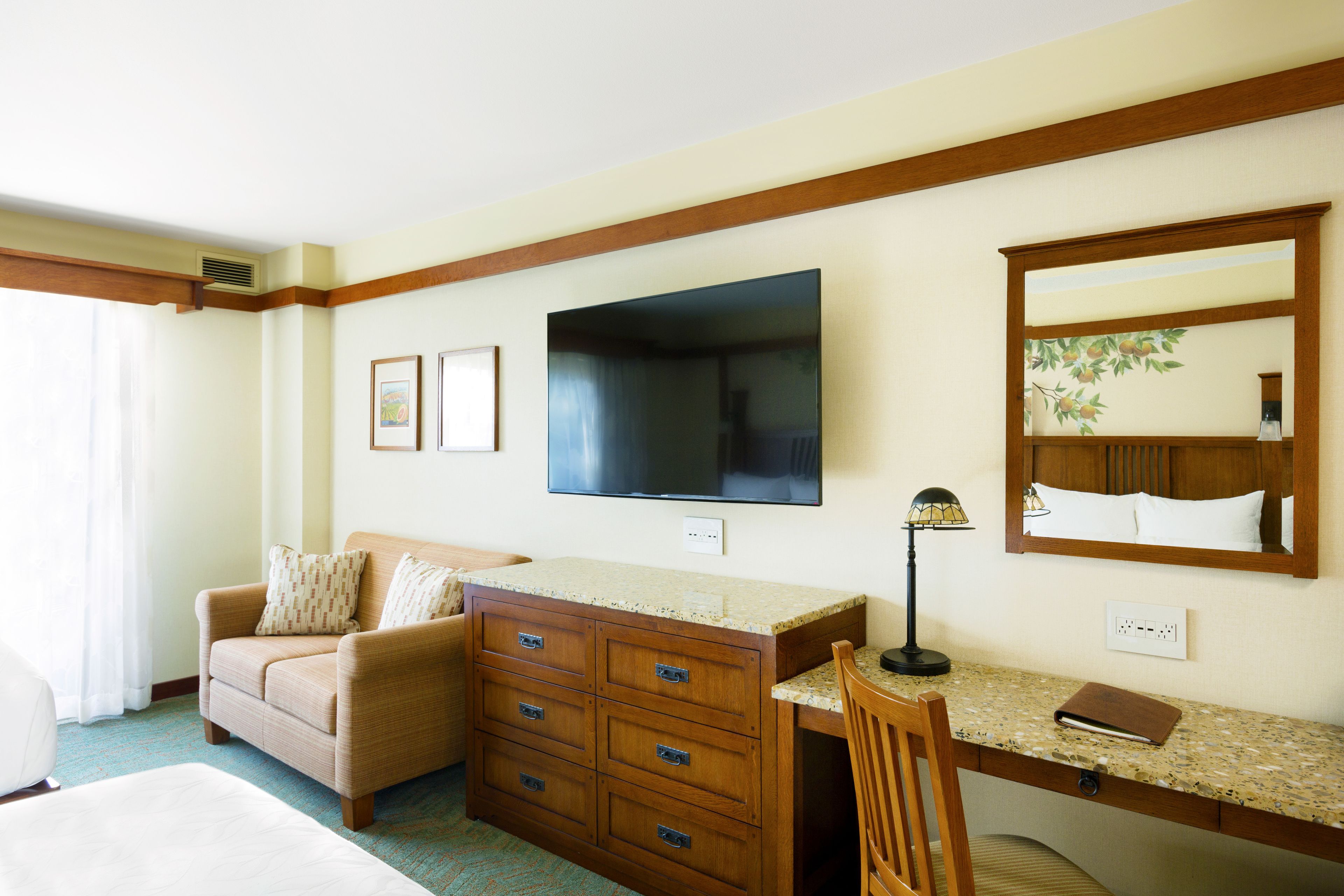 A hotel room with a wooden desk, a sofa, a television, and a mirror.