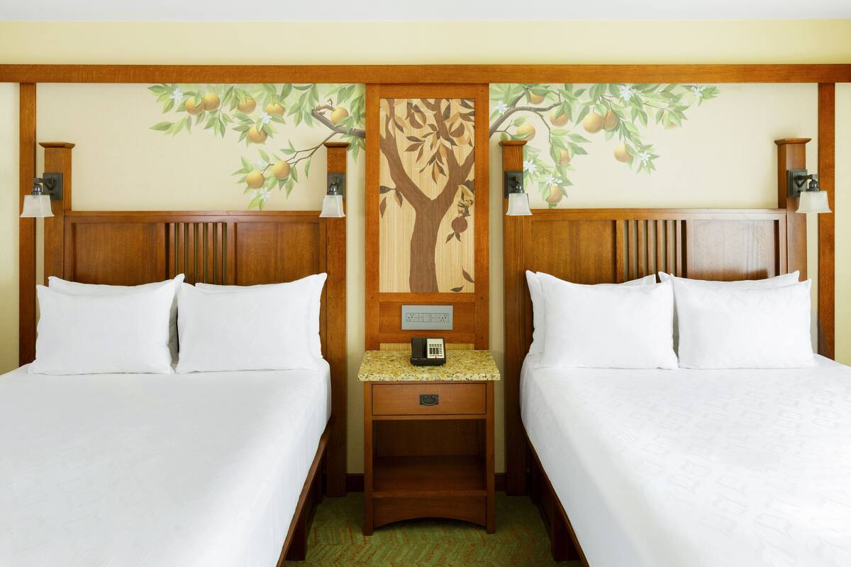 Een hotelkamer met twee bedden, een houten hoofdbord met een boomdecoratie, nachtlampjes en een klein nachtkastje met een telefoon.