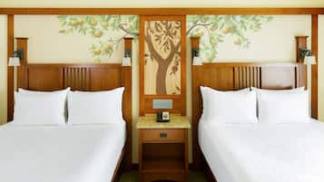 Camera d'albergo con due letti, una testiera in legno decorata con un murale di un albero, lampade da comodino e un piccolo comodino con un telefono.