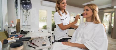 L'intérieur d'un salon de beauté, où une cliente est assise et une maquilleuse lui applique du maquillage.