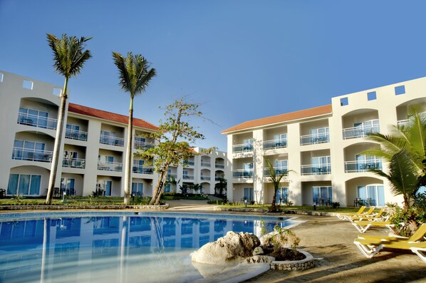 A hotel with a swimming pool, palm trees, and lounge chairs. - Cofresi Palm Beach & Spa Resort All Inclusive (Puerto Plata)