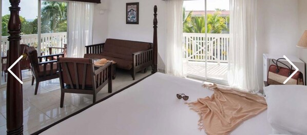 A bedroom with a bed, a chair, a small table, and a balcony with a white railing.
