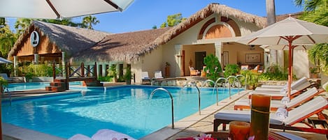 A poolside area with lounge chairs, a thatched-roof building, and a clear blue pool.