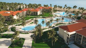 Un resort con varias piscinas, palmeras y vistas a la playa.