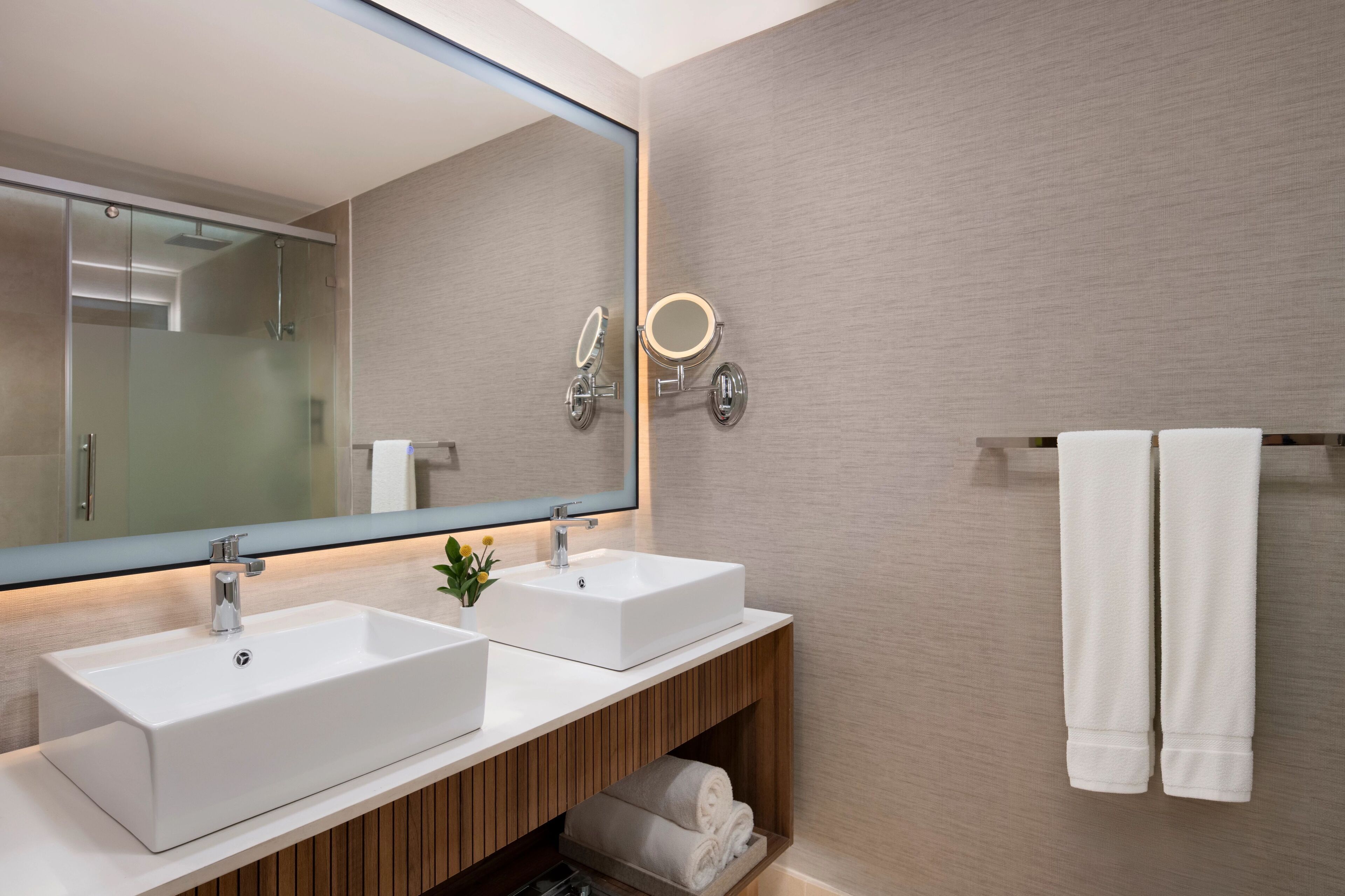 A modern bathroom with two sinks, a large mirror, and a towel rack.
