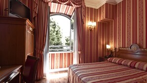 Ein Hotelzimmer mit einem großen Bett, einem Schreibtisch, einem Sessel, einem Fernseher und einem Fenster mit Vorhängen.