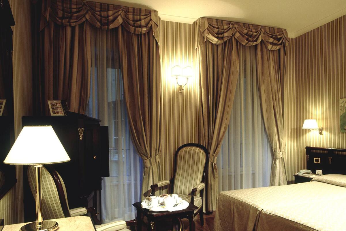 Une chambre d’hôtel comprenant un lit, un bureau avec un téléphone, une chaise et une lampe.