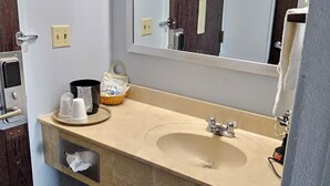 A bathroom with a beige sink, a mirror, a towel rack, and a trash bin. - Briarwood Inn of Sparta (Sparta)