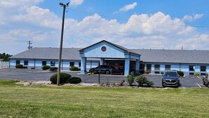 A motel with a blue exterior, a central garage entrance, and a parking lot with several cars. - Briarwood Inn of Sparta (Sparta)