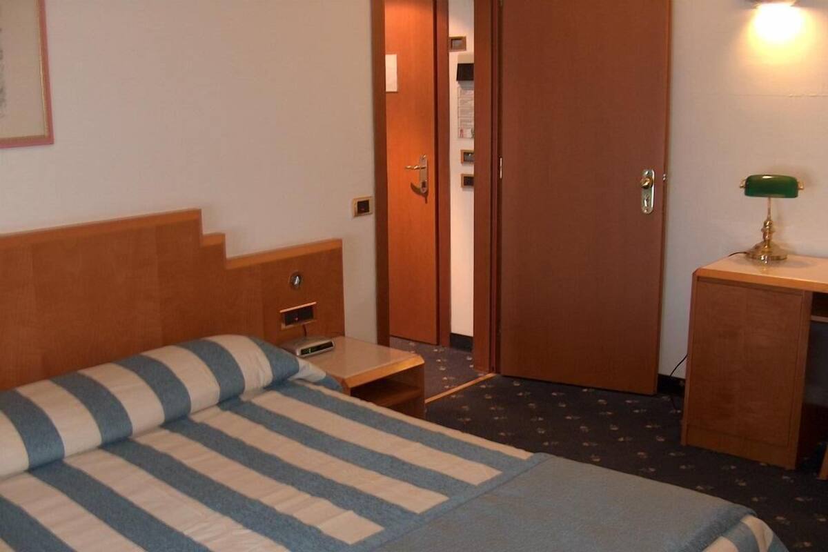 A hotel room with a bed, a desk, and a door.
