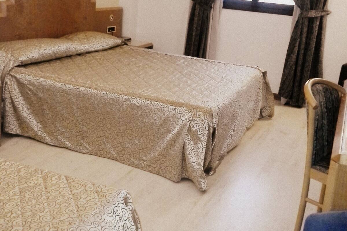 A hotel room with a bed, a chair, and a window with curtains.