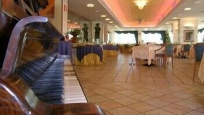 Um salão amplo com um piano, mesas e cadeiras dispostas para um evento.