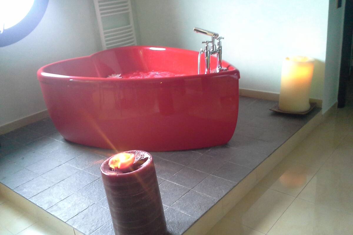 A red bathtub in a bathroom with a candle on the floor.