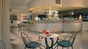 Um interior moderno com área de bar curva, assentos com cadeiras e uma mesa redonda, e uma cozinha visível ao fundo.