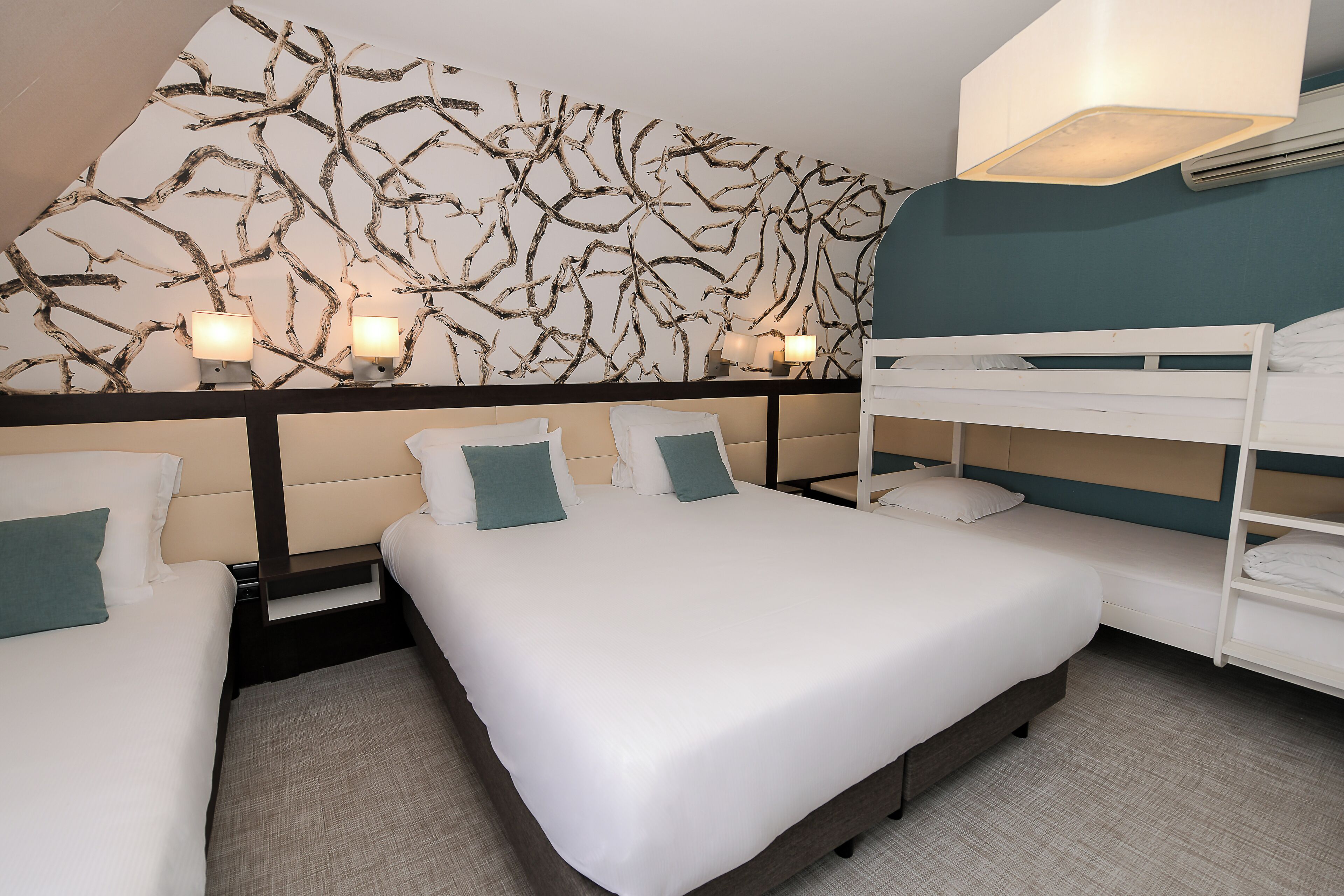 Camera d'albergo con un letto a castello, due letti singoli, una parete decorata con un motivo a ramo naturale e lampade da comodino.