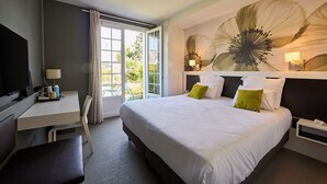 A hotel room with a large bed, a desk, a chair, a TV, and a window with curtains.