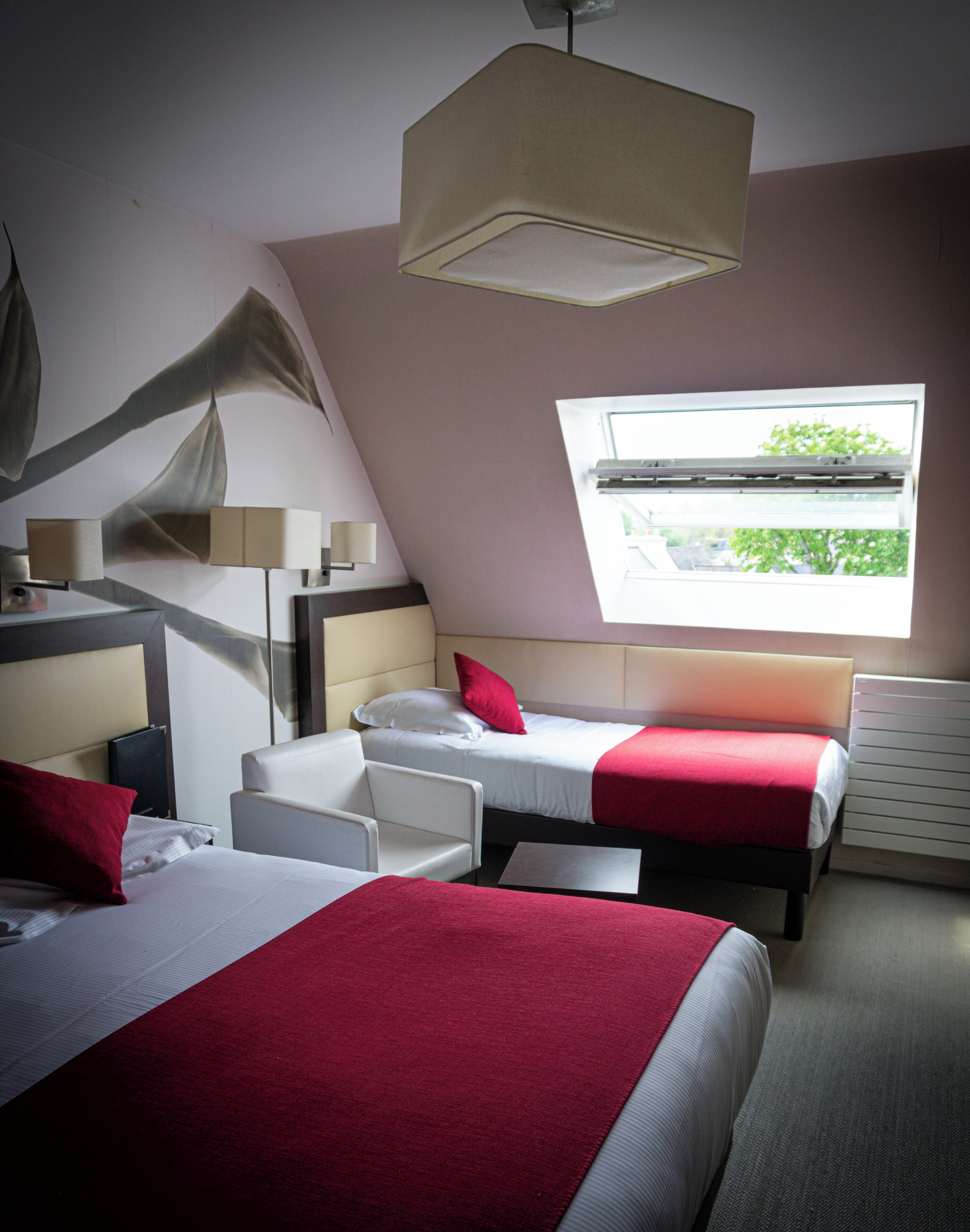 A hotel room with two beds, a desk, a chair, a window with a view, and a ceiling light.