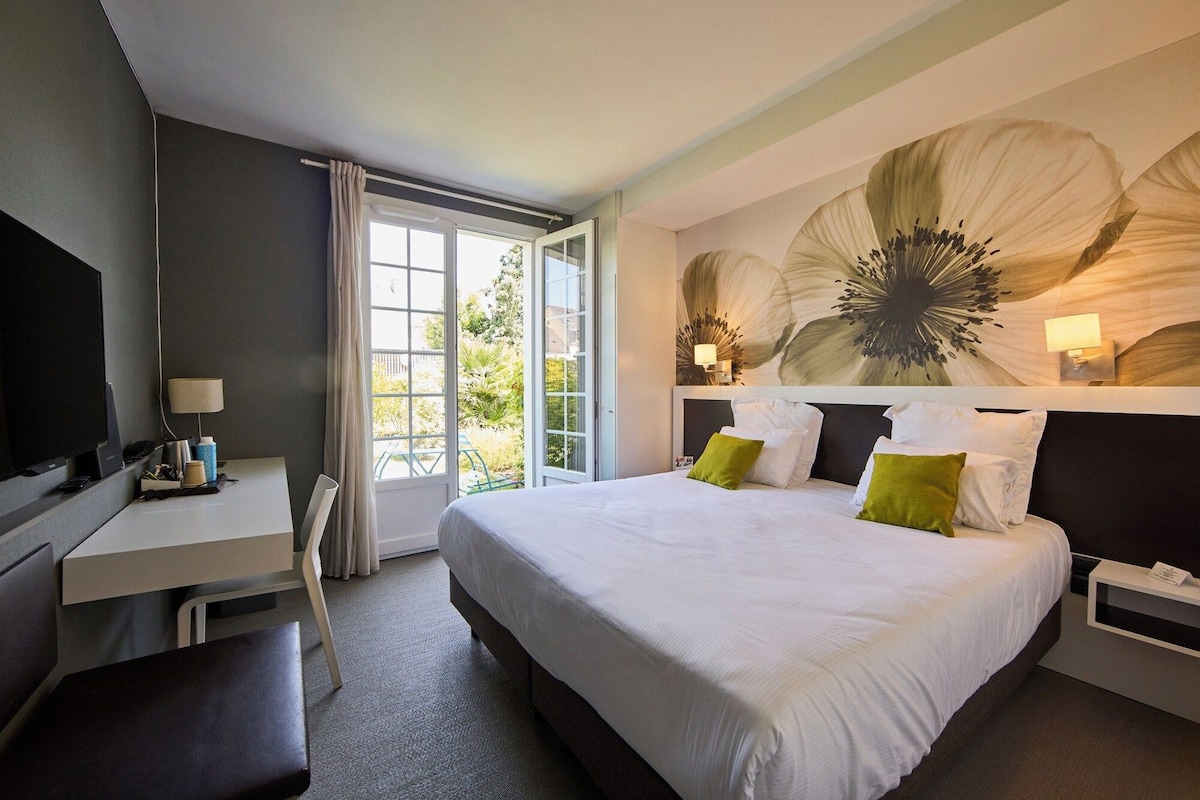 A hotel room with a bed, a desk, a chair, a TV, and a large window.