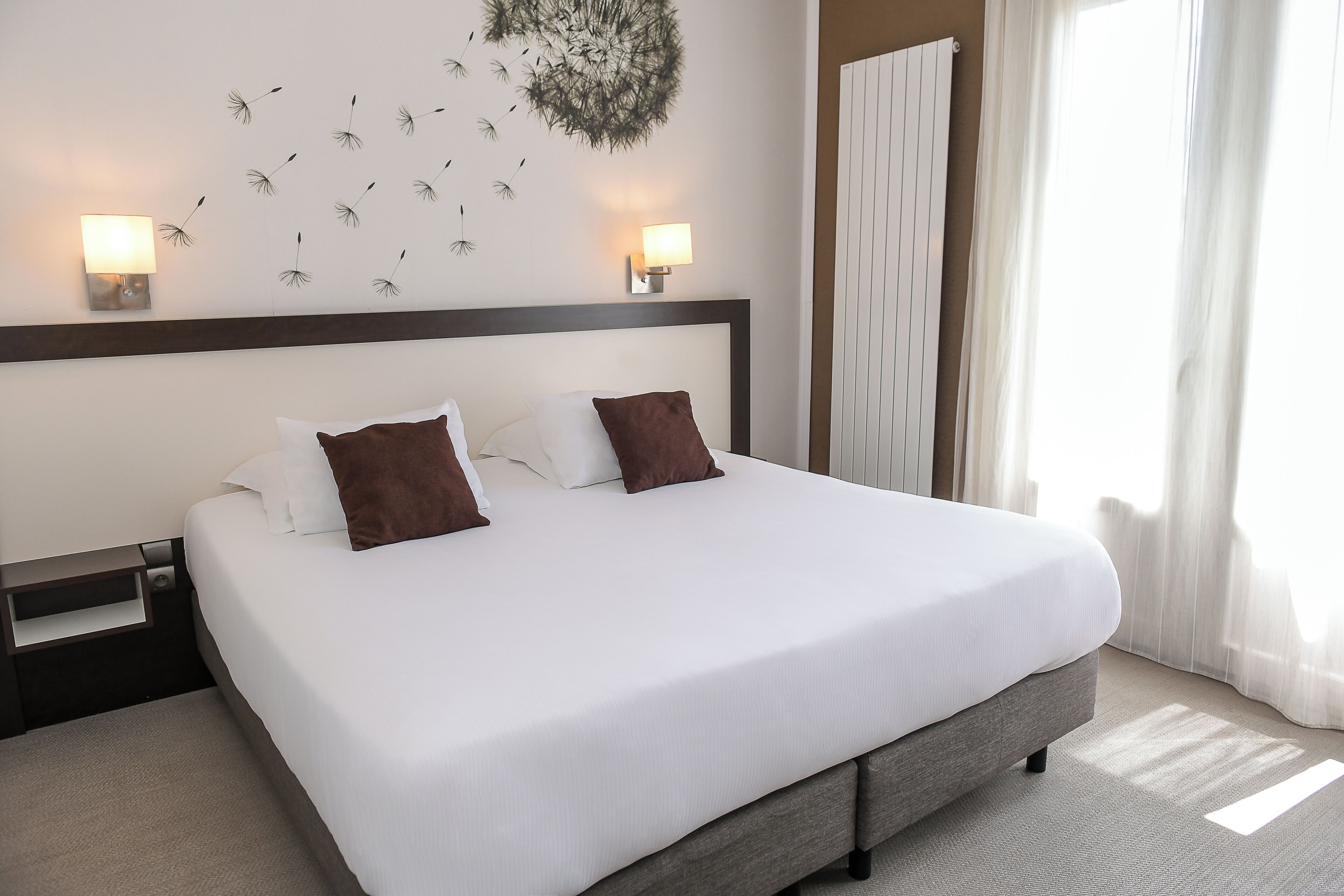 A hotel room with a large bed, two bedside lamps, a headboard, and a window with curtains.