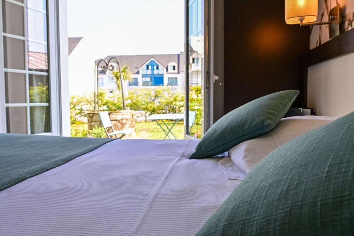 A hotel room with a bed, a green pillow, and a view of a building with blue windows.