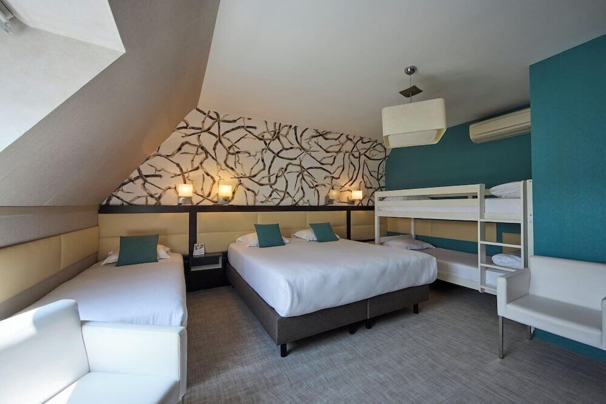 A hotel room with a bunk bed, two bedside tables, a sofa, and a wall with a unique design.