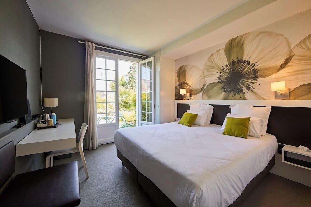 A hotel room with a bed, a desk, a television, and a large flower mural on the wall.
