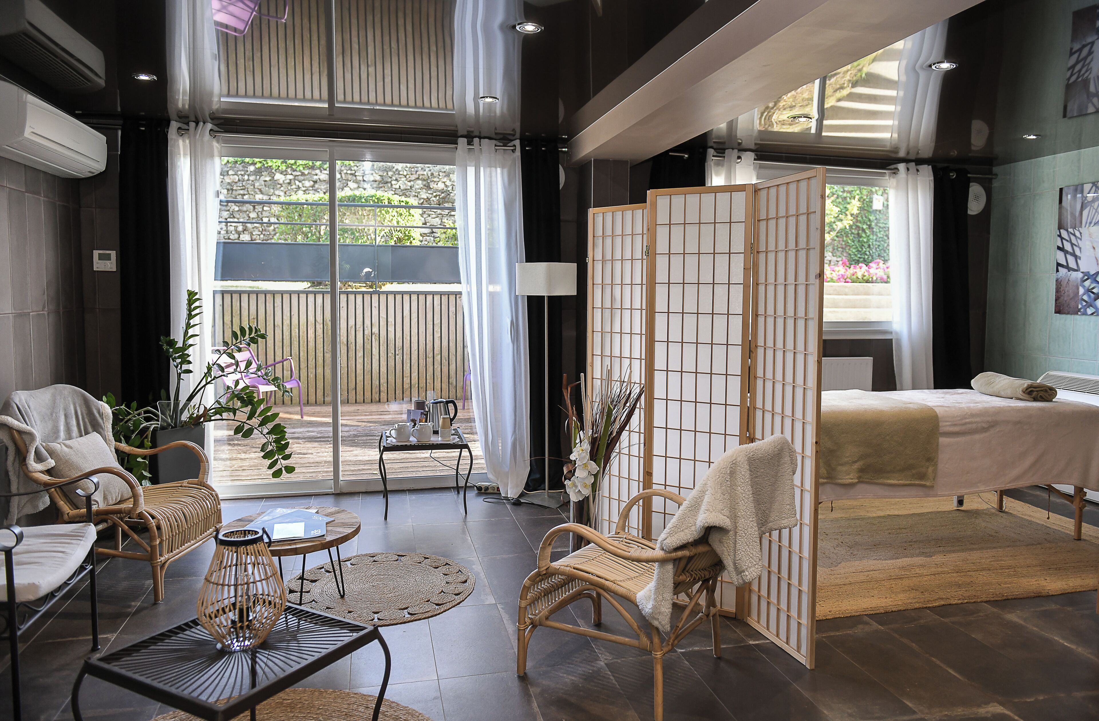 A modern hotel room with a balcony, wicker furniture, a bed, and a view of the outdoors.