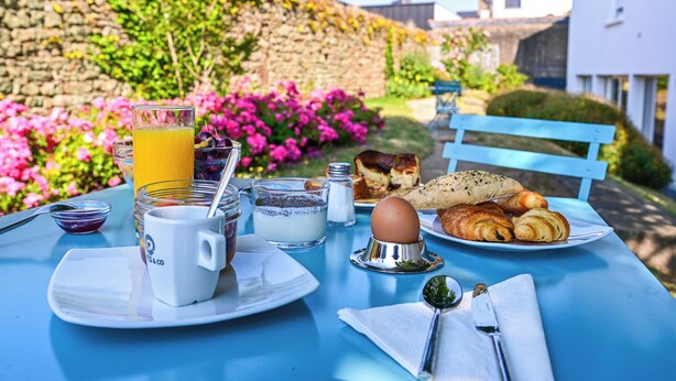 A breakfast table with a glass of orange juice, a cup, a plate with croissants, and a bowl of yogurt.