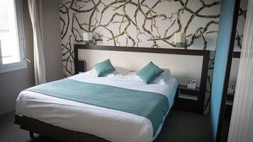 Una cama bien tendida con dos almohadas, una mesita de noche con una lámpara y una pared con un motivo de ramas.