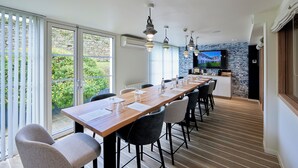 A modern dining area with a long wooden table, black and grey chairs, and pendant lighting.