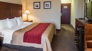 A hotel room with a large bed, a bedside lamp, a television, and a desk with a chair.