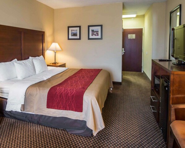 A hotel room with a large bed, a bedside lamp, a television, and a desk with a chair.