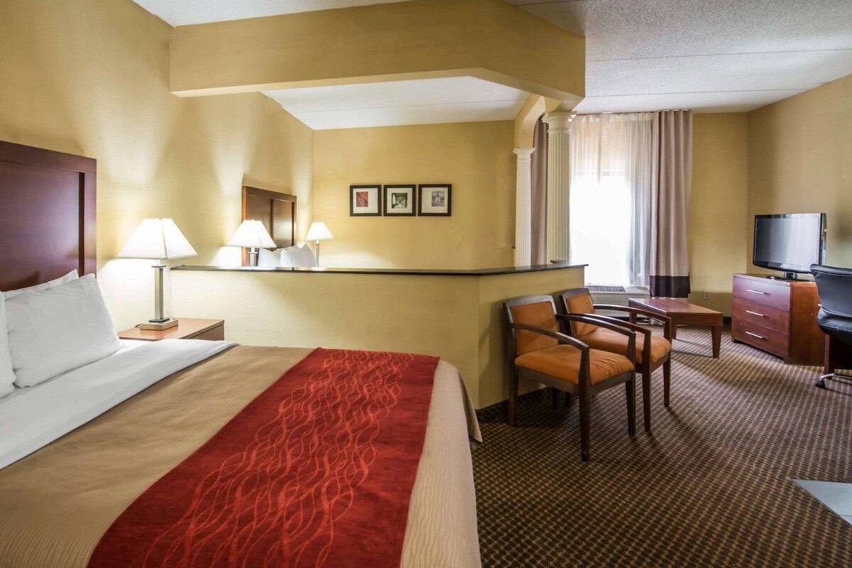 A hotel room with a bed, a desk, two chairs, a television, and a window with curtains.