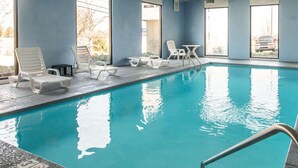 Piscina interna com espreguiçadeiras e mesa, grandes janelas e um letreiro com a palavra 'Welcome'.
