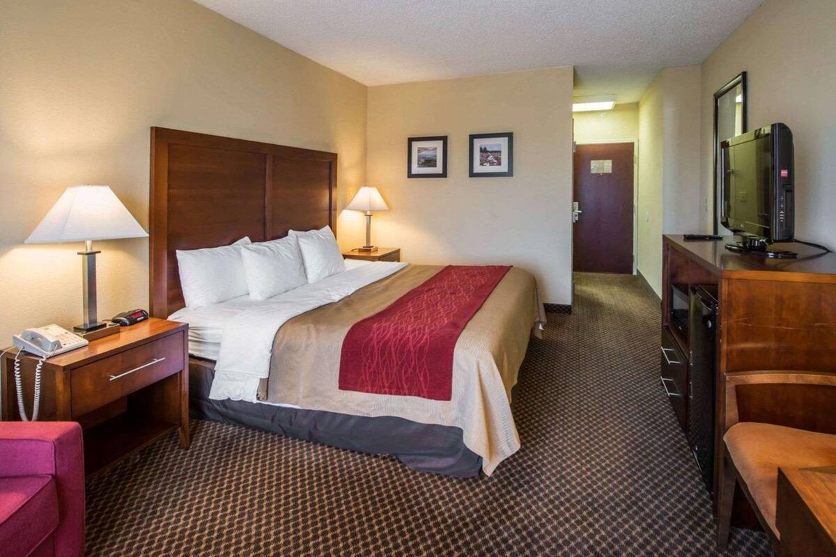 A hotel room with a bed, bedside lamps, a desk with a telephone, a television, and a door leading to another room.