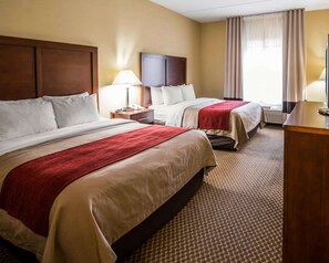A hotel room with two beds, a nightstand with a lamp, a desk, and a window with curtains.