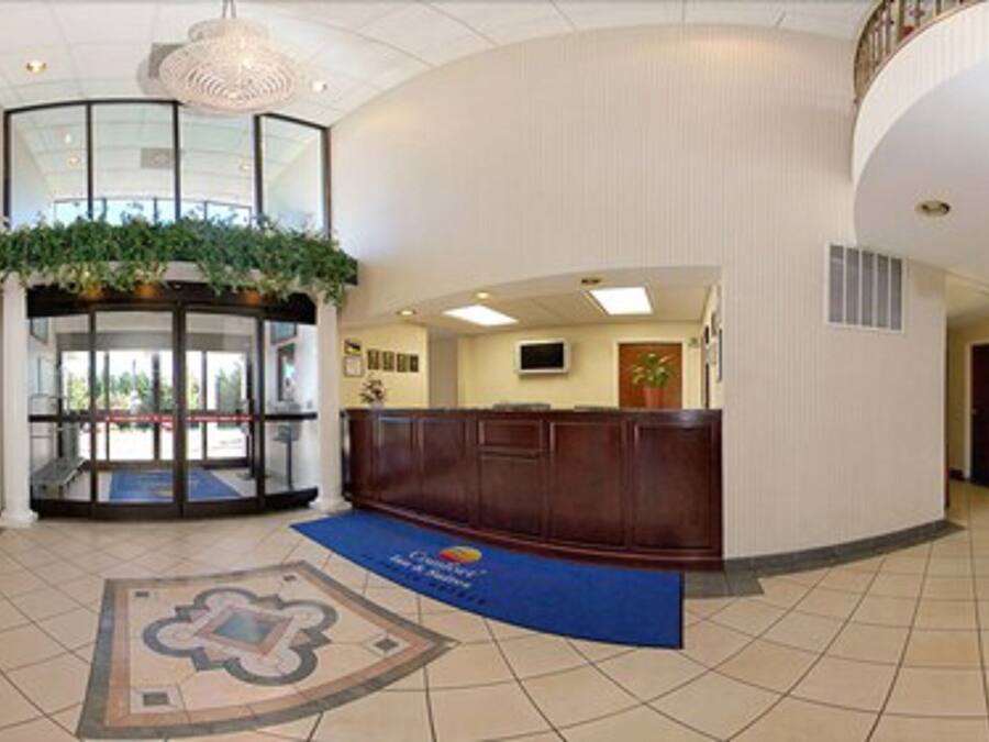 A hotel lobby with a reception desk, a glass door entrance, a large chandelier, and a patterned floor.