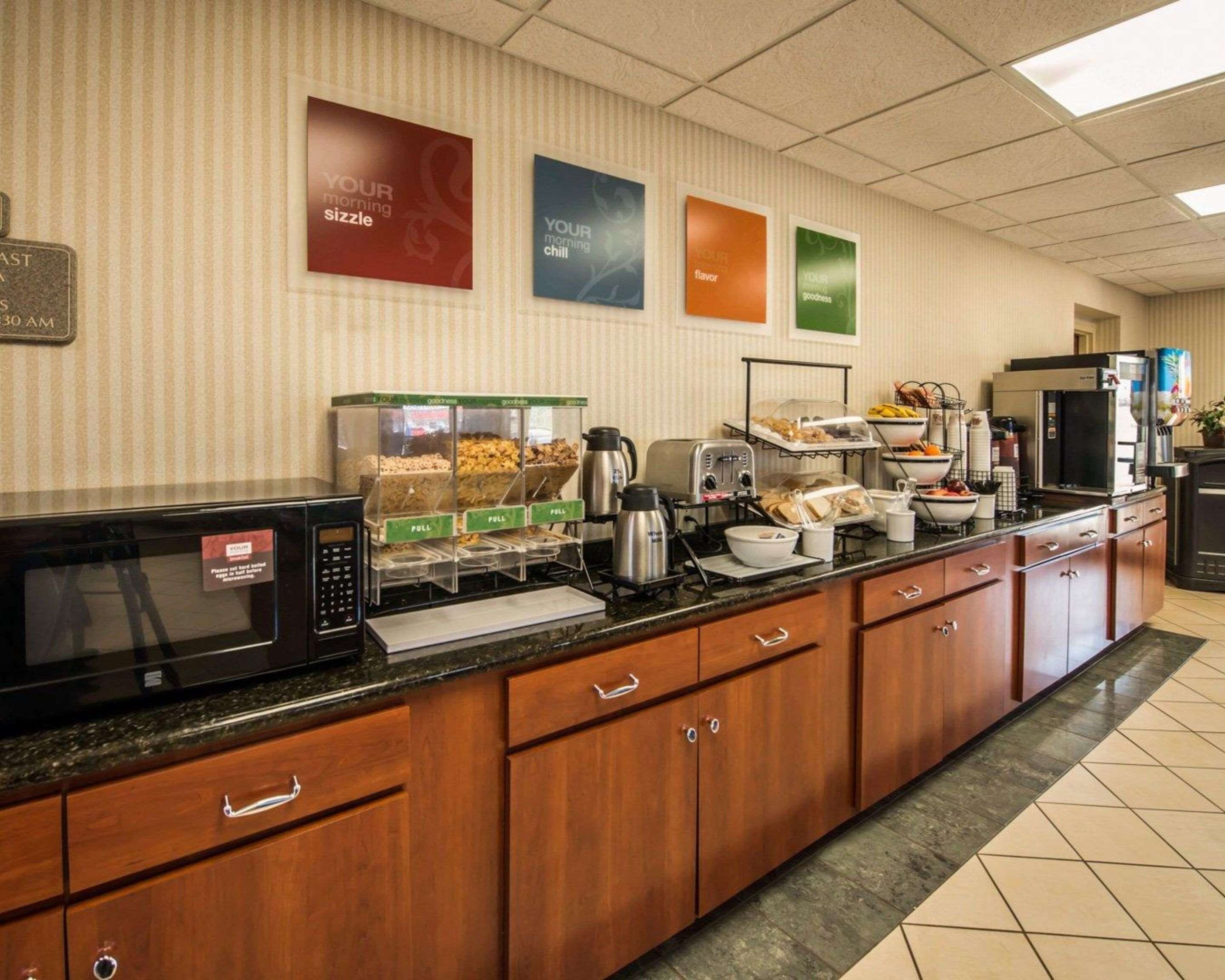Ein Frühstücksbereich in einem Hotel mit einer Mikrowelle, einer Kaffeemaschine und verschiedenen Speisen an einem Buffet.