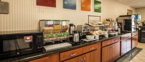 A hotel breakfast area with a microwave, coffee maker, and various food items on a buffet counter.