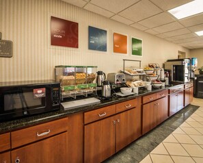 A hotel breakfast area with a microwave, coffee maker, and various food items on a buffet counter.
