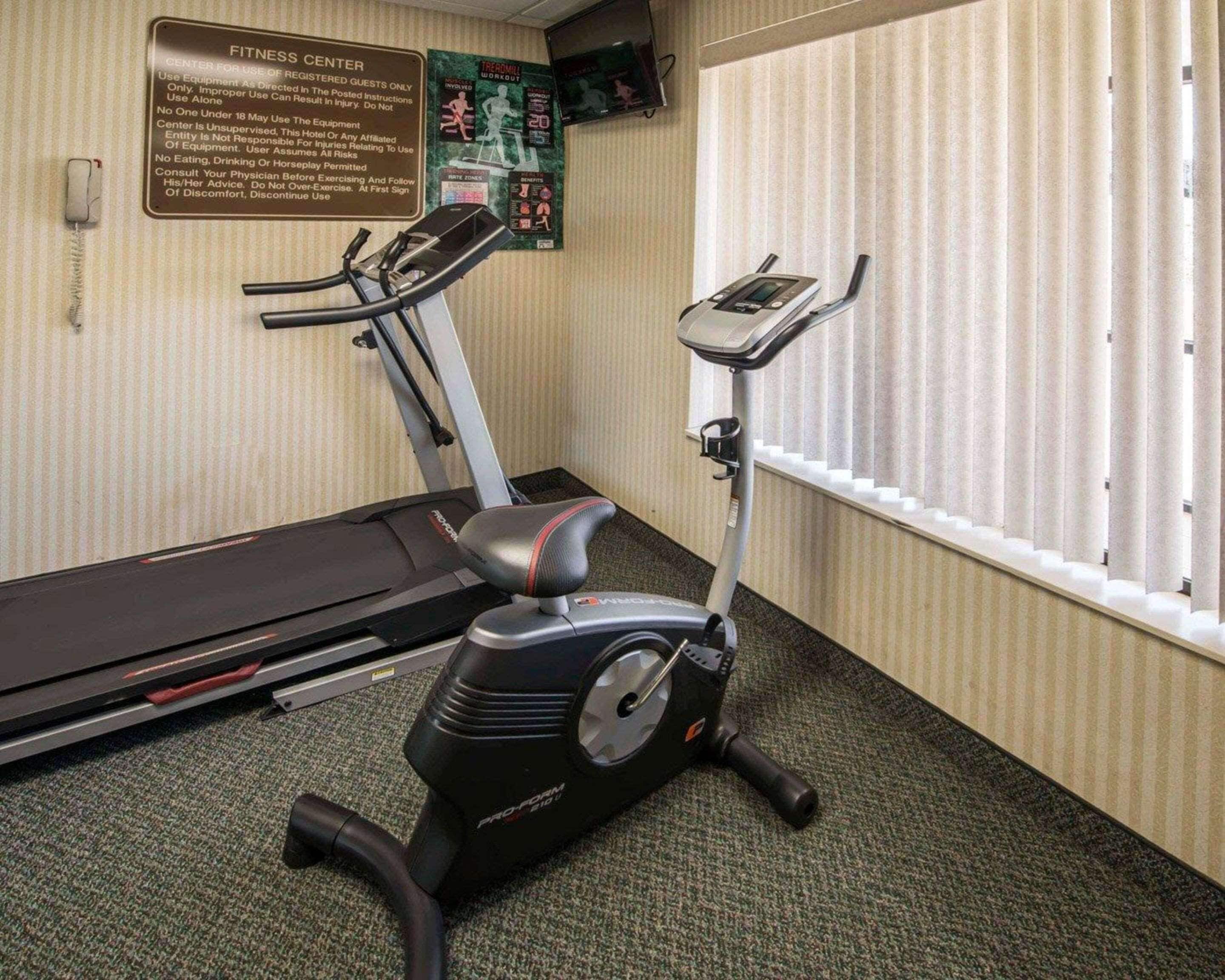 Un gimnasio con una cinta de correr, una máquina elíptica y un cartel en la pared.