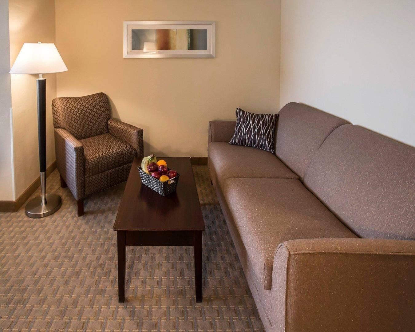 Een hotelkamer met een gestreept fauteuil, een bank, een bijzettafeltje met fruit en een vloerlamp.