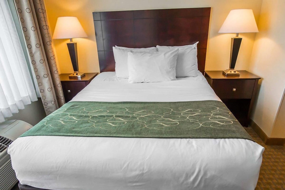 A hotel room with a large bed, two bedside lamps, a green decorative throw, and a window with curtains.