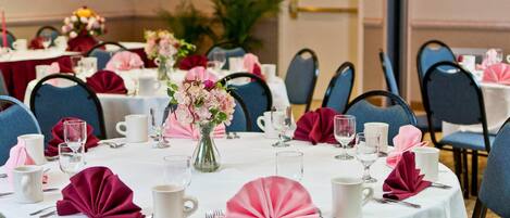 A round table with white tablecloths, pink napkins, and a vase of flowers.