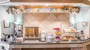 A buffet counter with a coffee station, fruit bowls, and a variety of food items.