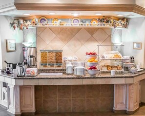 Un mostrador de buffet con una estación de café, fuentes de fruta y una variedad de alimentos.